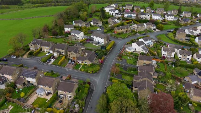 A reversing drone shot over the Rockwood Drive estate in Skipton, North Yorkshire, revealing well-kept gardens, stone houses and green fields of Aireville Park beyond. Spring footage.