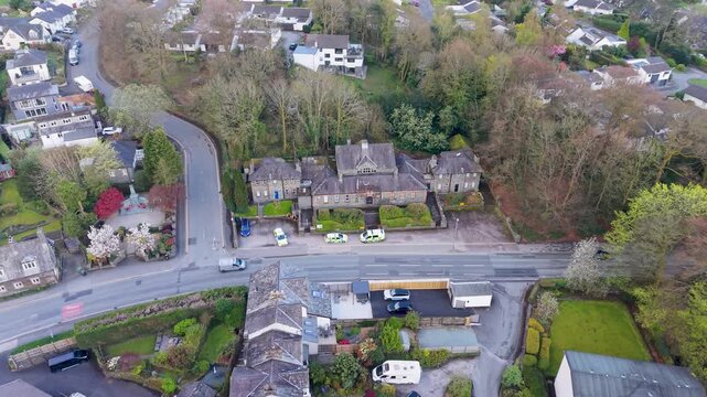 A drone descends over Windermere Police Station, built in traditional Lake District slate, as a police car reverses into a parking spot with two others already outside. Cumbria, England.