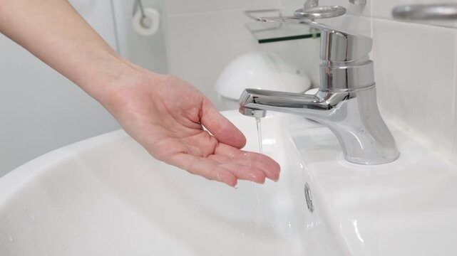 Hand under faucet with very weak water flow, low pressure tap water problem in sink, close up