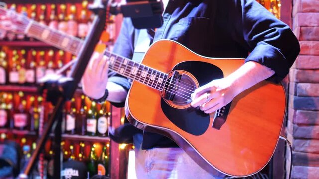 Close up of acoustic guitar player performing live music in bar with microphone and warm lights nightlife atmosphere.