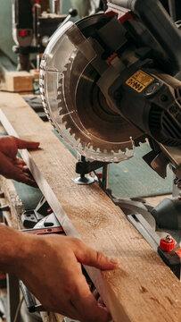 Carpeting process. Woodwork service. Male joiner hands holding timber near circular miter saw with safety cover. Power steel electric equipment workshop.