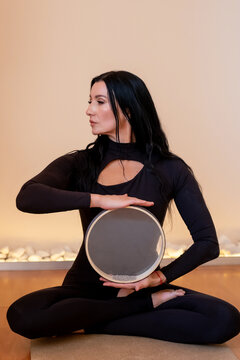 Relaxation practice. Sound healing. Calm woman doing balance atmosphere ritual holding frame drum for concentration session in yoga studio.