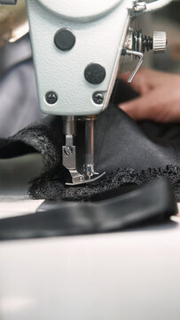 Clothing production. Sewing lace. Dressmaker hands attaching garnish to black fabric corset. Manufacturing industry professional equipment.