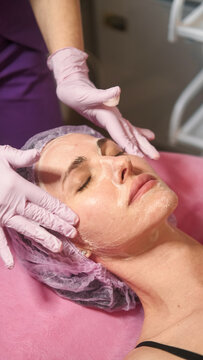 Facial care. Beauty treatment. Professional cosmetologist hands cleansing woman skin on table for skincare procedure in spa salon.