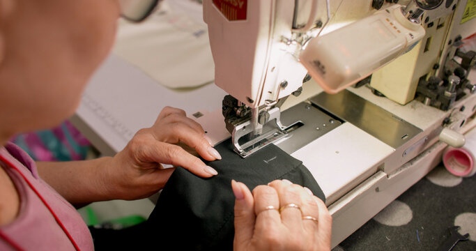 Clothing making. Sewing process. Tailor working on stitching professional machine. Woman creating buttonhole on black fabric sleeve.