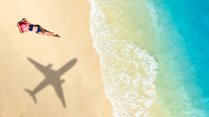 Top view of a woman in bikini blue sunbathing on white sand beach with a large airplane shadow over her  concept of dream summer vacation, air travel, and tropical island holiday destination.   © Media 
