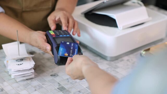 Senior entrepreneur cafe owner barista hold POS machine to customer, Asian female in apron welcome warmly in counter, croissants and glassware background, retired elderly woman start small business