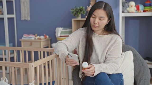 Woman holding smartphone and pill bottle, checking label beside a crib in a baby nursery building; concern caregiving.