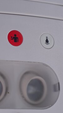 Vertical close-up of an airplane overhead panel with illuminated attendant call icon, reading light button, and cabin fixtures in soft neutral light.