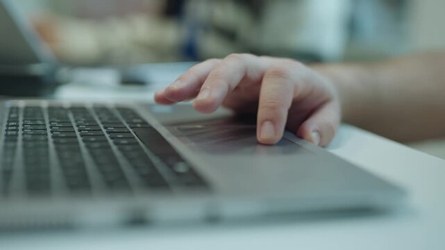 Close-up shot of fingers using a laptop trackpad during computer work at a desk in an office setting.
