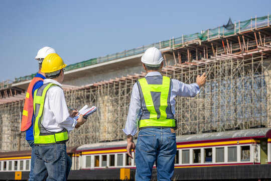 Professional civil engineers and site managers monitoring infrastructure development and railway project, Group of asian construction workers in hardhats discussing skyway project near railway station