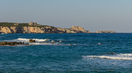 Fototapeta premium Waves gently lapping against the rocky coastline under a serene sky at golden hour.