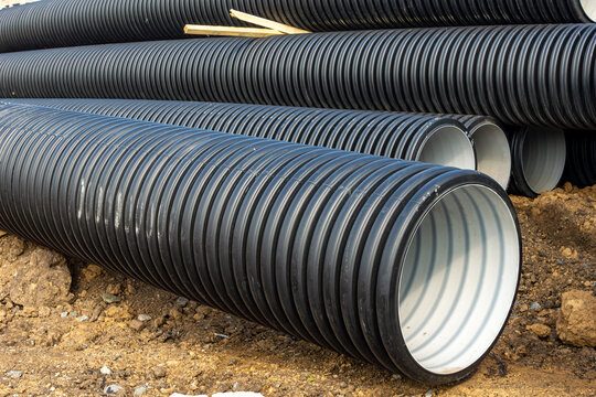 Closeup of large diameter corrugated plastic pipes with black ribbed exterior and smooth interior for underground drainage systems