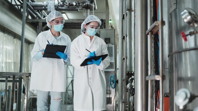 Two female industrial engineers coworkers inspect and examine quality control, production machines in food manufacturing factory, clean and protective uniforms for maintenance, and evaluate operation.