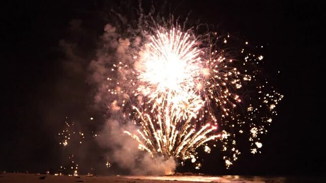 Low Angle Golden and Magenta Fireworks Display Over Dark Empty Beach