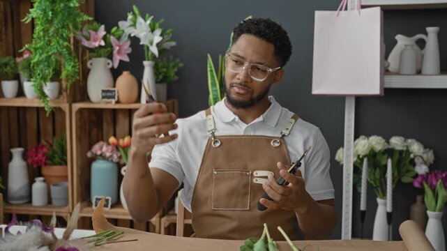 Man florist in apron carefully holds pruning shears and wire cutters, inspecting blades and grip in studio; concentration.