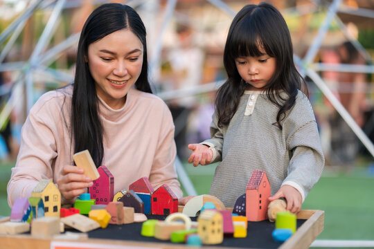 mother and preschool child girl playing with wooden toy block at outdoor