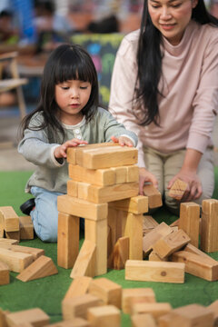 mother and preschool child girl playing with wooden toy block at outdoor
