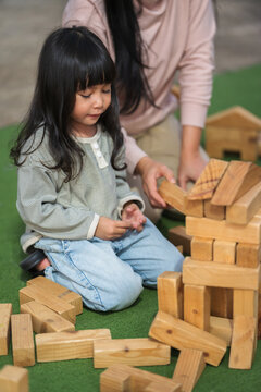 mother and preschool child girl playing with wooden toy block at outdoor