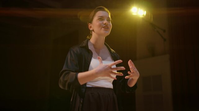 Confident woman delivering an emotional stage performance under dramatic theater lighting, expressing passion and intensity during a powerful solo presentation