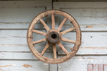 Obraz premium Weathered wooden wheel hangs on rustic white siding