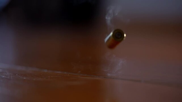 One bullet shell casing falls to wooden surface in slow motion. Fired brass casing bouncing after shot, close up action detail.