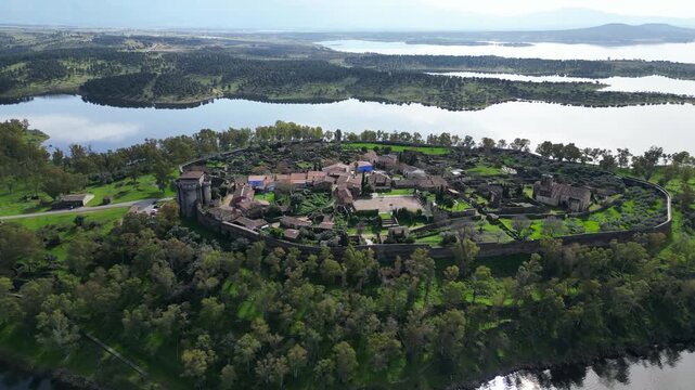 Drone view of Granadilla walled village in Spain with reservoir, islands and distant mountains, showing historic town surrounded by water and nature.