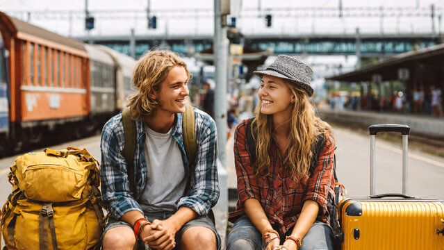 Group of young friends waiting at train station platform with luggage, smiling and chatting before departure, railway transport, casual lifestyle, travel concept