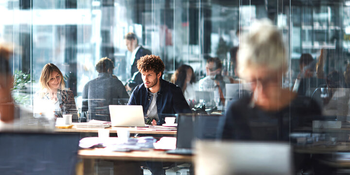 Busy modern office environment with diverse business people multitasking, collaborating, team members using laptops, smartphones and documents, networking and communication.
