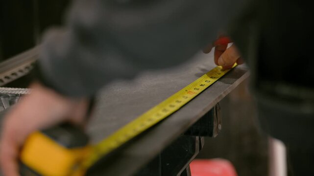 Worker measuring and marking a tile for cutting. The person uses a marker and measuring tape to ensure accurate sizing.