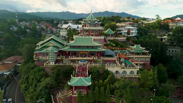 Aerial orbiting descent over Cebu Taoist Temple revealing multi-tiered Chinese pagoda rooftops, red staircases with lanterns, dragon ornaments, and tourists on terraces