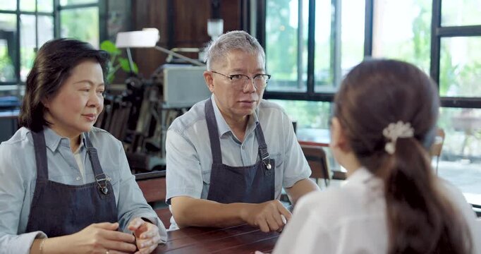 Elderly asian husband wife guide young barista, explain daily tasks, teamwork cooperation builds confidence, family entrepreneurs strengthen cafe service standard create strong small business