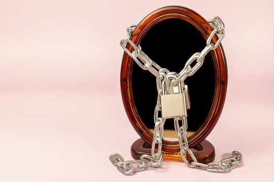 Mirror with chains and a padlock symbolizing a trapped identity, insecurity, and mental health challenges against a pink background