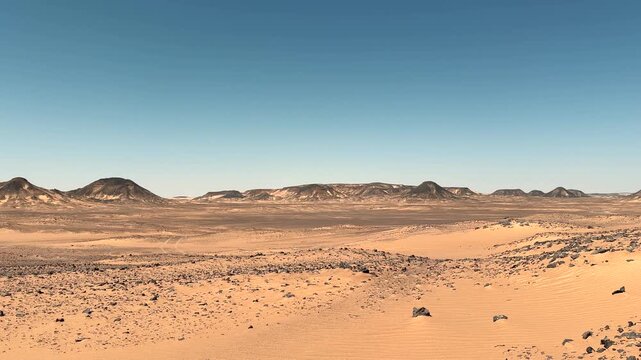 Wide desert landscape with black volcanic hills and scattered basalt stones in the sand