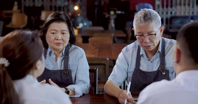 Asian senior entrepreneurs discuss service improvement with barista team, husband wife plan daily operation, encourage collaboration, enhance customer satisfaction, maintain warm teamwork environment