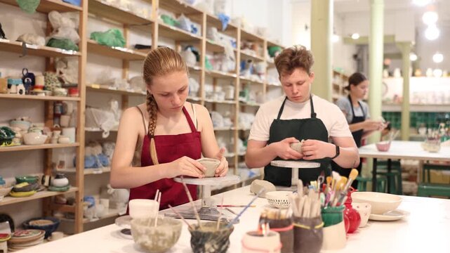 Teenage girl attentively learns how to make pottery with a wooden sticker in the workshop. High quality 4k footage