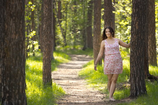 A young woman walking in the forest. A smiling woman stands barefoot near a pine tree.