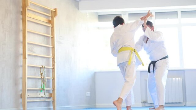 Individual judo lesson for teenager - guy and trainer are sparring in the gym