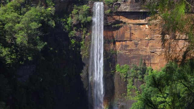 Fitzroy Falls, a stunning waterfall, falling over a colorful rock face and causing swirling rainbow colors near the bottom in Morton National Park in Kangaroo Valley in New South Wales, Australia.