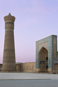 Kalyan Minaret and Mir-i-Arab Madrasah at twilight in Bukhara, Uzbekistan. Empty Poi Kalyan square with ornate brickwork and turquoise tilework under a pastel sky. Ideal for travel and heritage.