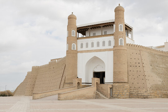 Ark Fortress entrance gate in Bukhara with massive brick walls and twin towers under an overcast sky. Ideal for travel guides, heritage publications, and tourism marketing materials.