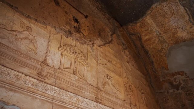 Preserved Pompeii wall fresco showing delicate Roman decorative painting with architectural motifs and small mythological figures inside an ancient interior.