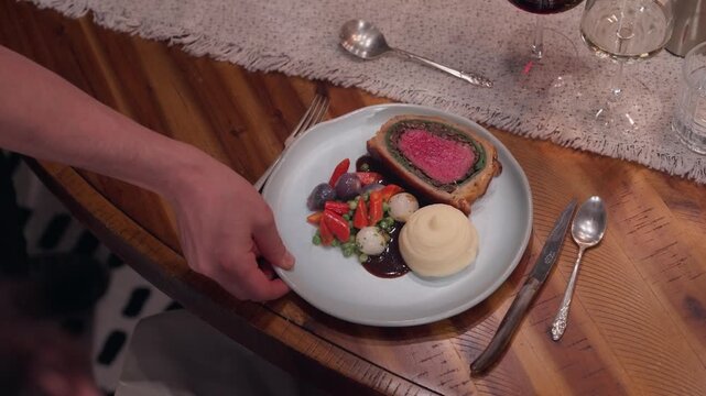 A rustic Beef Wellington dinner is presented at the table of a private dining experience (slow motion 4K).