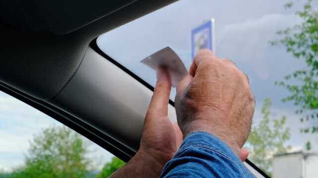 Unrecognizable man hands placing vignette sticker on car windshield from inside, preparing vehicle for road use, transport regulation and travel concept.