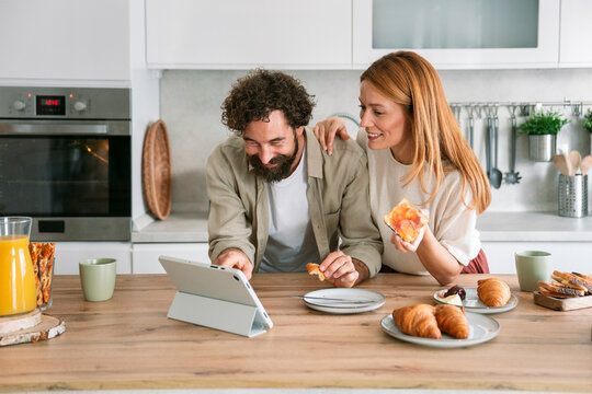 Couple smiling and using digital tablet during breakfast in kitchen