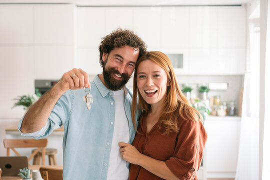 Happy couple holding new home keys and smiling in modern kitchen