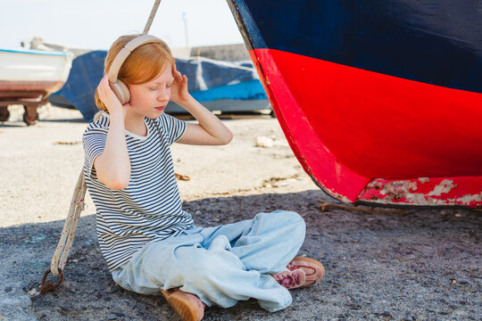 Child with headphone listening to music sitting by a boat