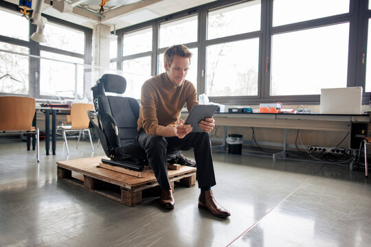 Engineer using tablet PC sitting on chair over pallet at workshop