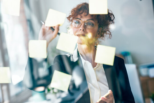 Businesswoman planning strategy with sticky note on glass window