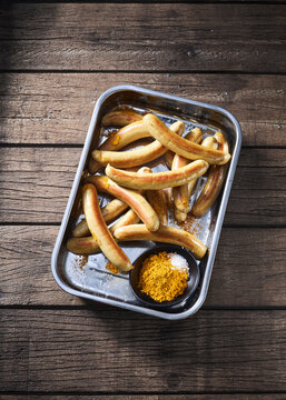 Grilled sausages in a tray with curry powder and salt on wood